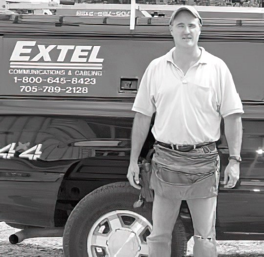 A photo of the owner of Extel in front of his truck which displays the company logo